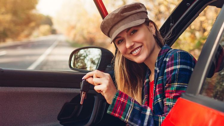 Junge Frau lacht im Auto und zeigt den Autoschlüssel